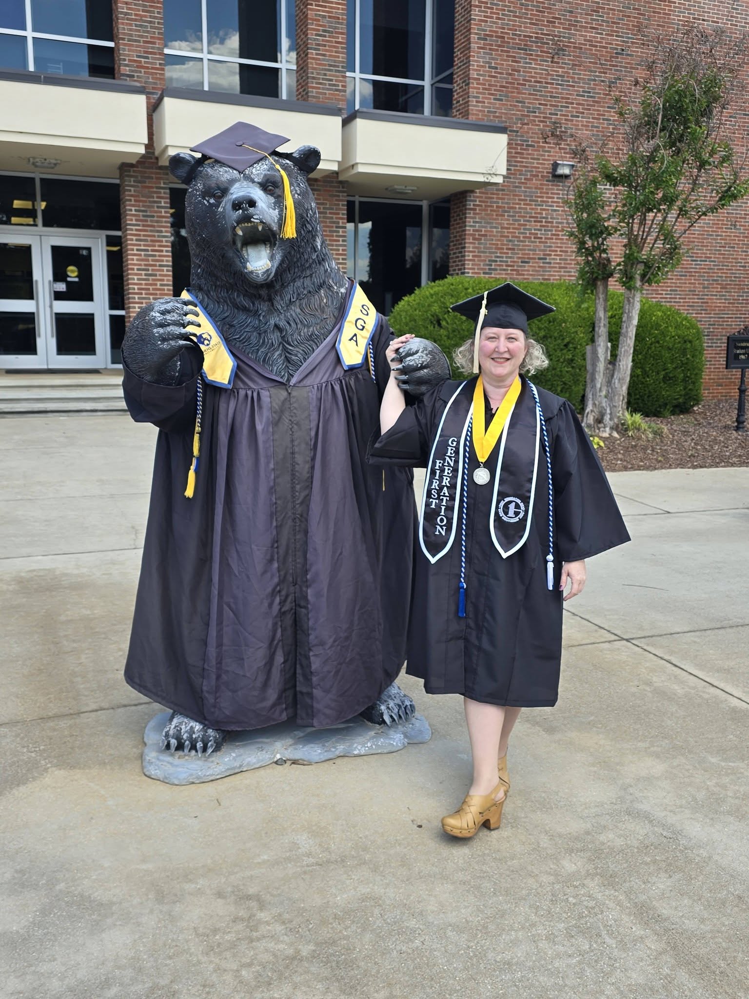 Tonya Sidelinger in graduation attire beside a costumed bear statue